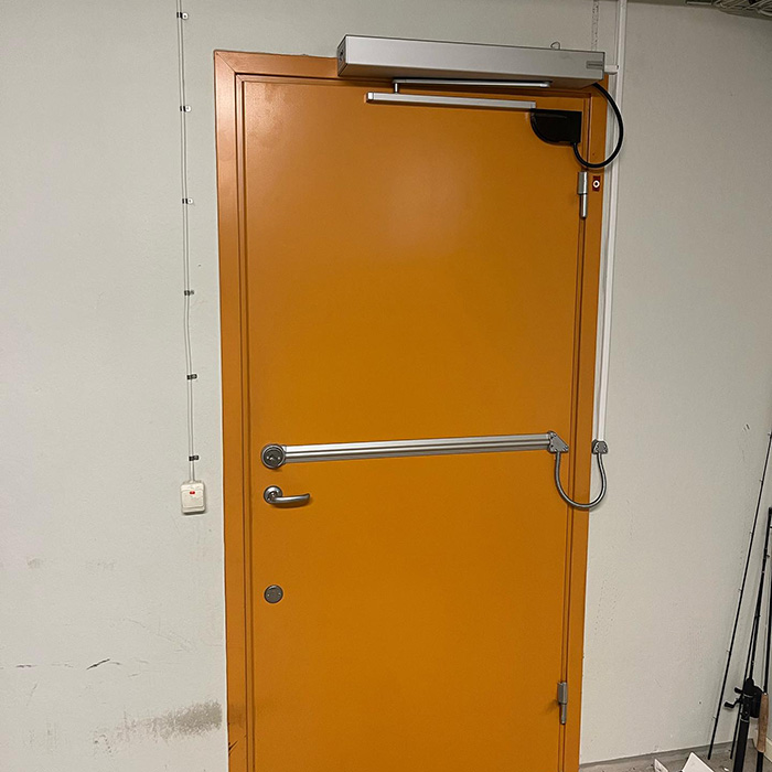 En orange dörr med automatisk dörröppning, leder till ett cykelförråd där cyklar förvaras tryggt och säkert.